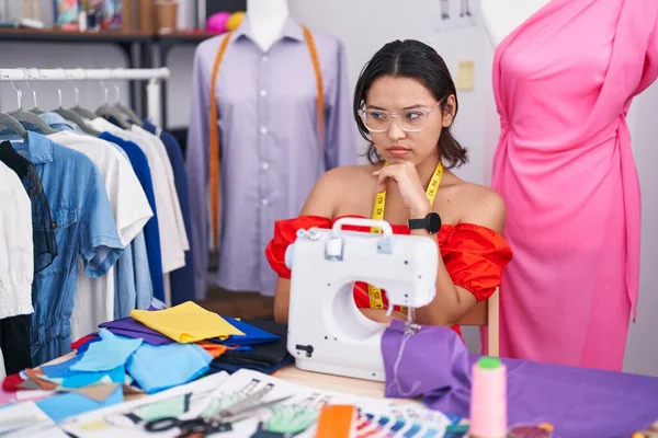 Hispanic Young Woman Dressmaker Designer Using Sewing Machine Thinking Worried — Stockfoto