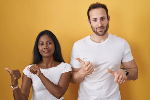 Interracial Couple Standing Yellow Background Pointing Back Hand Thumbs Smiling — 图库照片