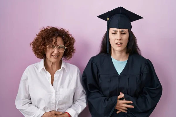 消化不良 痛みを伴う病気が具合が悪いので ヒスパニック系の母親と娘は 胃の上に手で卒業キャップと式のローブを着て キャッシュ コンセプト — ストック写真