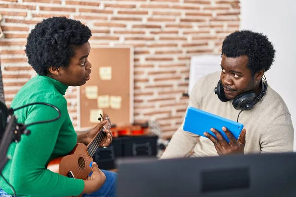 African american man and woman music group using touchpad playing ukelele at music studio