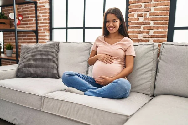 Młoda Latynoska Kobieta Ciąży Dotyka Brzucha Siedząc Kanapie Domu — Zdjęcie stockowe
