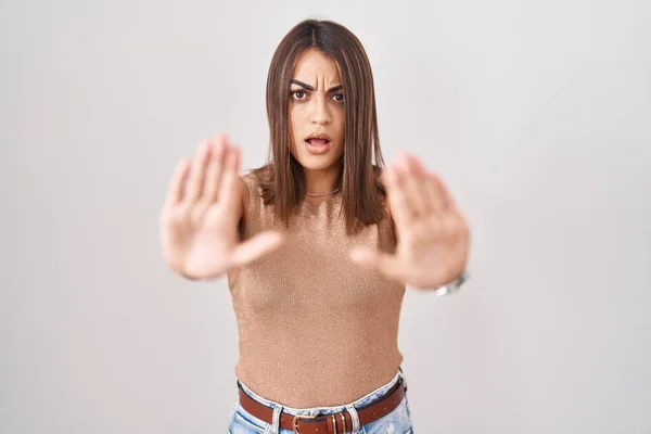 Young hispanic woman standing over white background doing stop gesture with hands palms, angry and frustration expression