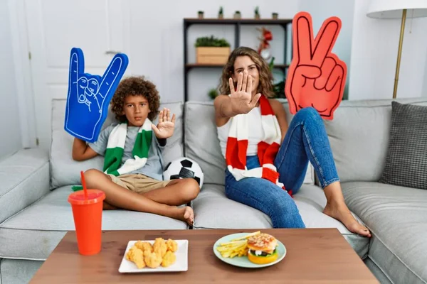 Young woman and son football hooligan cheering game with open hand doing stop sign with serious and confident expression, defense gesture