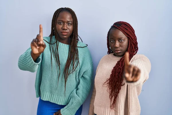 Две Африканки Стоят Синем Фоне Показывая Пальцем Вверх Сердитым Выражением — стоковое фото