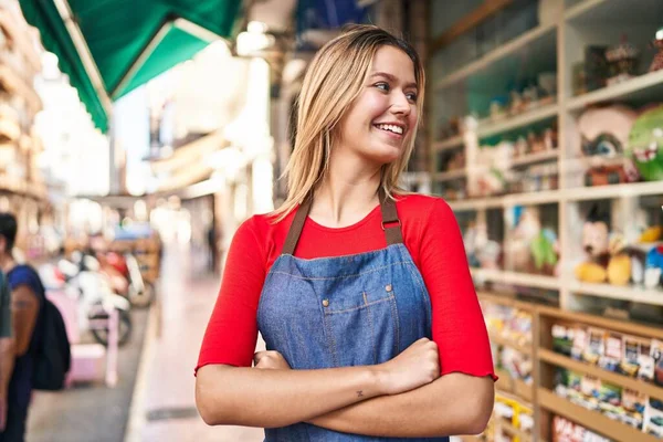 Young hispanic woman shop assistant standing with arms crossed gesture at street