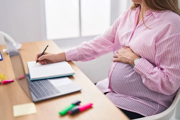 在办公室里 年轻的怀孕女工在笔记本上写着摸肚皮的话 — 图库照片