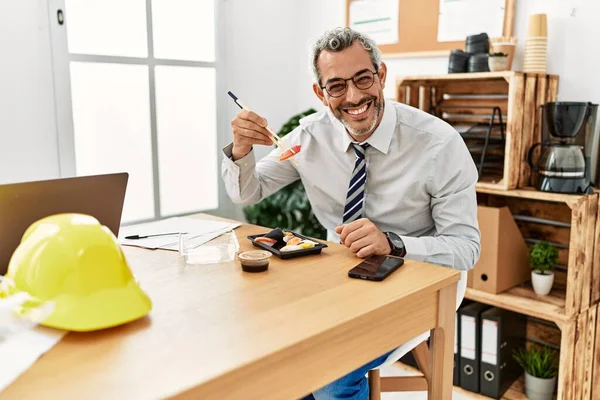 中年白髪の建築家が自信を持って笑顔で寿司を食べるオフィス — ストック写真