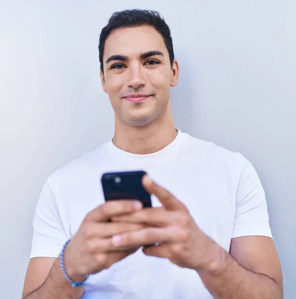 Joven Hombre Hispano Sonriendo Confiado Usando Teléfono Inteligente Sobre Fondo —  Fotos de Stock