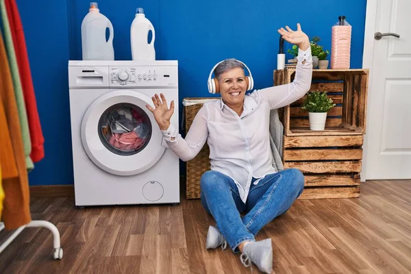 洗濯室で洗濯機を待っている音楽を聞いている中年の女性 — ストック写真
