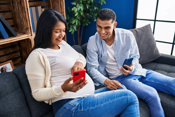 Young Latin Couple Expecting Baby Using Smartphone Sitting Sofa Home — Photo