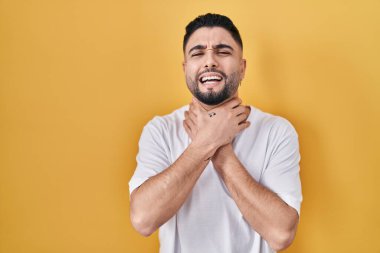 Sarı arka plan üzerine gündelik tişört giyen genç yakışıklı adam bağırıyor ve boğuluyor çünkü acı verici bir boğulma var. Sağlık problemi. Boğulma ve intihar konsepti. 