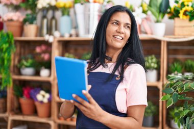 Orta yaşlı İspanyol çiçekçi kadın çiçekçiye dokunarak gülümsüyor.