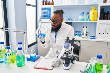 Bilim adamı üniforması giyen genç Afro-Amerikan adam laboratuarda test tüpü tutuyor.