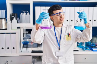 Young non binary man scientist smiling confident measuring liquid at laboratory