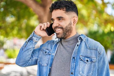 Genç İspanyol adam gülümsüyor. Parktaki akıllı telefondan konuşuyor.