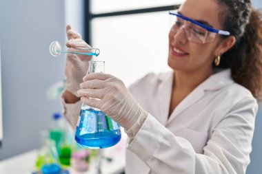 Genç ve güzel İspanyol bilim kadını laboratuarda test tüpüne sıvı döküyor.