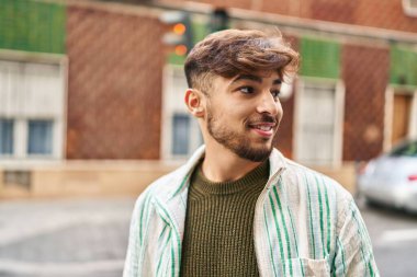 Genç Arap adam gülümsüyor. Kendinden emin. Caddenin kenarına bakıyor.