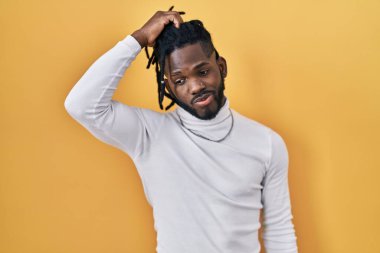 Sarı arka plan üzerine balıkçı yaka kazak giyen Afrikalı bir adam kafasını karıştırıyor ve soru soruyor. Şüpheyle kararsız, kafa kafaya düşünerek. Düşünceli kavram. 