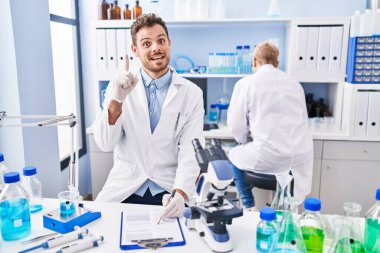 Hispanic man and woman working at scientist laboratory smiling with an idea or question pointing finger with happy face, number one 