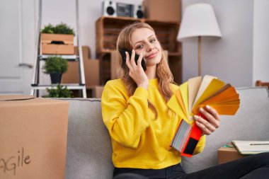 Young blonde woman talking on smartphone choosing color at new home