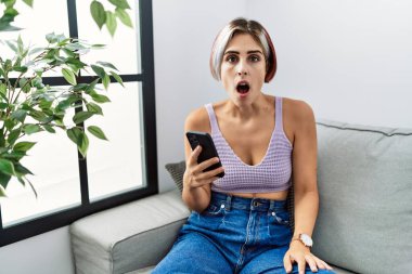 Genç ve güzel bir kadın koltukta oturmuş, şok olmuş bir şekilde mesaj yazıyor. Şüpheci ve alaycı görünüyor. 