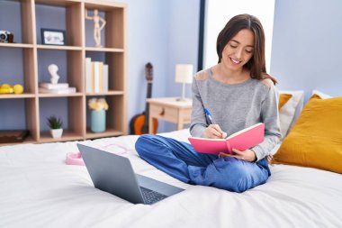 Genç, güzel, İspanyol bir kadın öğrenci kitap yazıyor. Yatak odasında ders çalışıyor.
