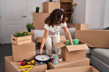 Middle age hispanic woman packing boxes at new home