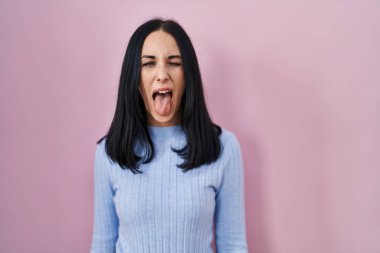 Hispanic woman standing over pink background sticking tongue out happy with funny expression. emotion concept. 