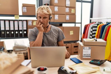Young blond man wearing operator headset working at online shop looking stressed and nervous with hands on mouth biting nails. anxiety problem. 
