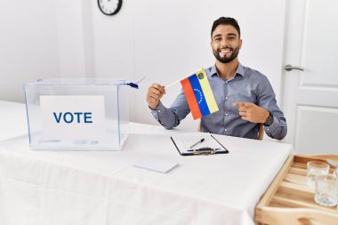 Siyasi seçim kampanyasında sakallı genç yakışıklı adam elinde Venezuela bayrağı tutarken mutlu bir şekilde elini ve parmağını gösteriyordu. 