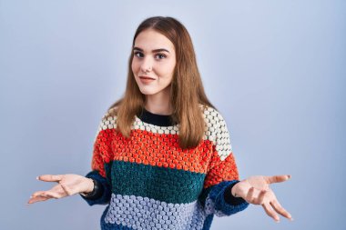 Young hispanic girl standing over blue background clueless and confused with open arms, no idea concept. 