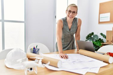 Young caucasian woman smiling confident writing on architect plan working at architecture studio