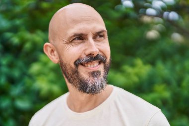 Genç kel adam parkın kenarına bakarak gülümsüyor.