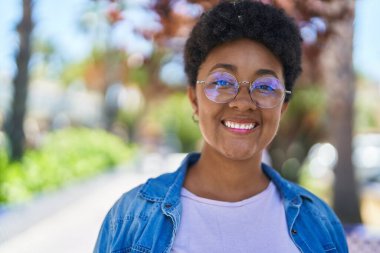 Afro-Amerikalı kadın parkta kendinden emin bir şekilde gülümsüyor.