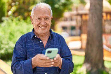 Senior grey-haired man smiling confident using smartphone at park