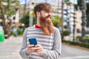 Young redhead man smiling confident using smartphone at street