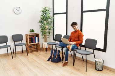 Young hispanic man smiling confident using laptop at waiting room