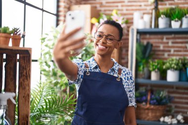 Afrikalı Amerikalı kadın çiçekçi çiçekçide akıllı telefondan selfie çekiyor.