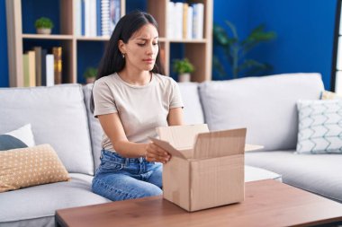 Young hispanic woman opening cardboard box skeptic and nervous, frowning upset because of problem. negative person. 