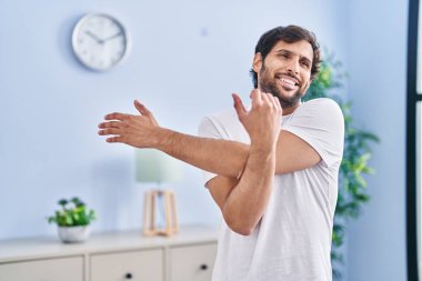 Young hispanic man smiling confident stretching at home