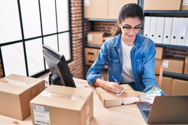 Genç ve güzel İspanyol kadın ecommerce iş işçisi. Ofisteki pakette akıllı telefon yazısını kullanıyor.