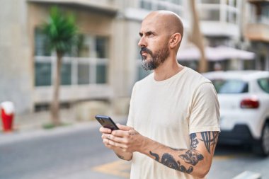 Genç kel adam akıllı telefon kullanıyor ve sokakta ciddi bir yüz ifadesi var.