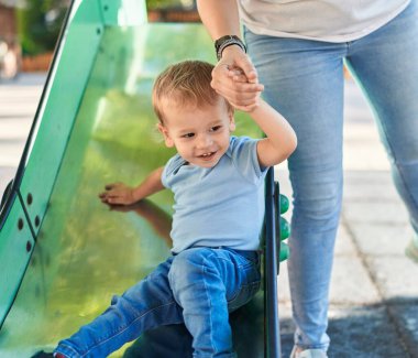 Anne ve oğlu parkta kayak yaparken kendinden emin bir şekilde gülümsüyor.