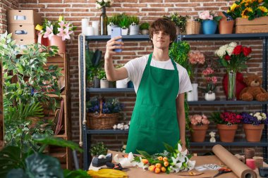 Genç sarışın çiçekçi çiçekçide akıllı telefondan selfie çekiyor.