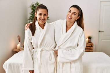 İki kadın bornoz giyiyor. Güzellik merkezinde birbirlerine sarılıyorlar.