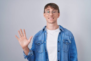 Caucasian blond man standing wearing glasses showing and pointing up with fingers number five while smiling confident and happy. 