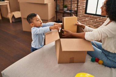 Mother and son unpacking cardboard box sitting on sofa at new home