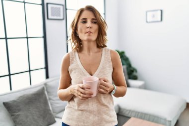 Orta yaşlı bir kadın evde kahve içiyor dudaklarıyla balık suratı yapıyor, çılgınca ve komik bir jest. Komik ifade. 