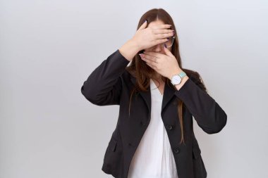 İş ceketi ve gözlük takan güzel esmer kadın gözlerini ve ağzını elleriyle kapatıyor, şaşırmış ve şok olmuş. duygu gizleme 