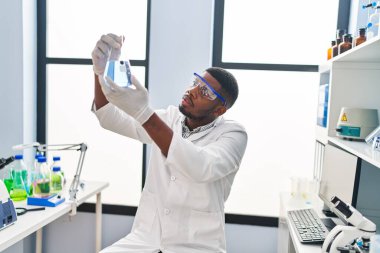 Bilim adamı üniforması giyen genç Afro-Amerikan adam laboratuarda test tüpü tutuyor.